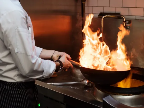 Woman chef cooking with a wok and a large flame coming out of the wok