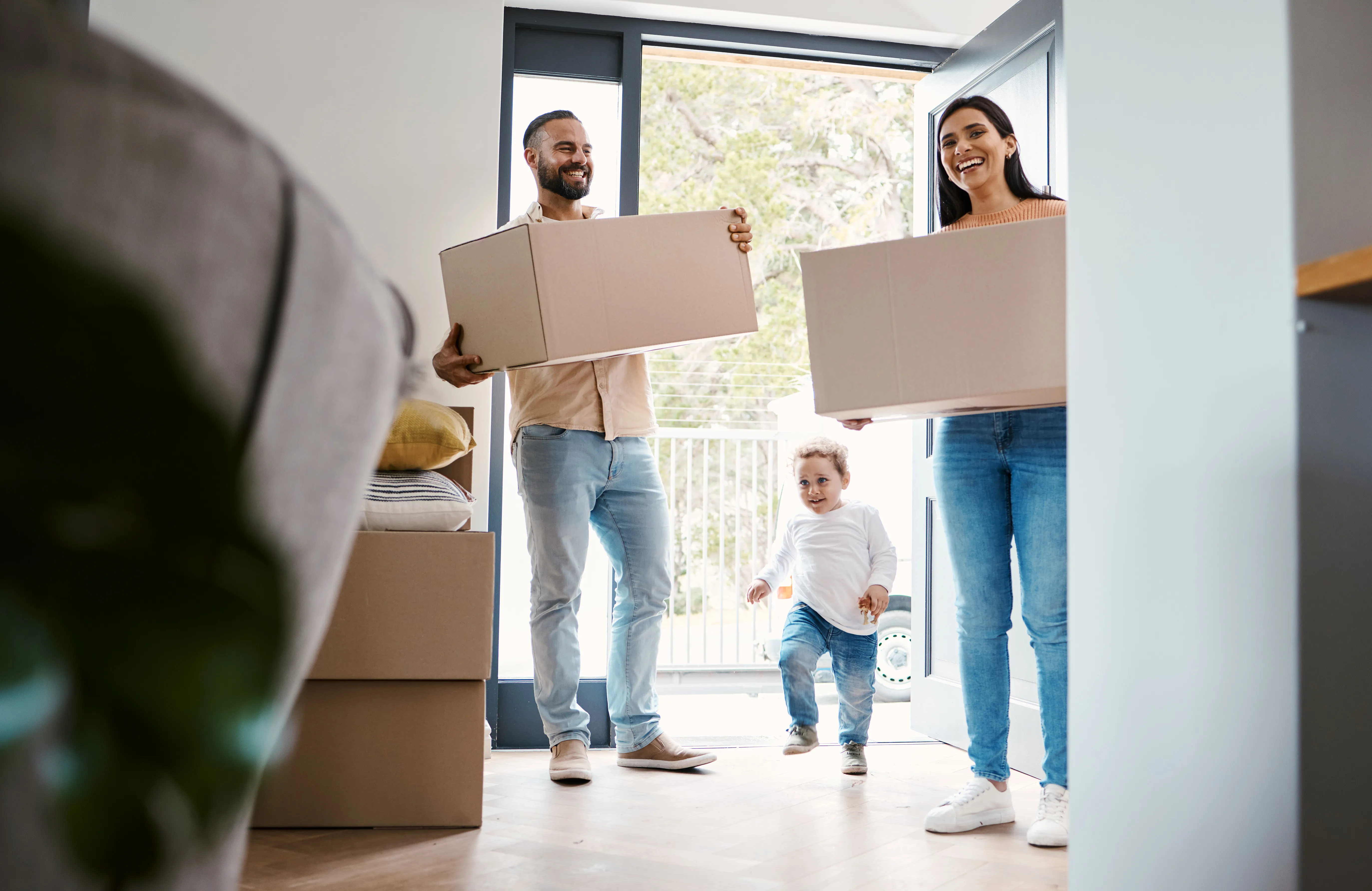 Couple holding boxes and moving into a house with their toddler son.