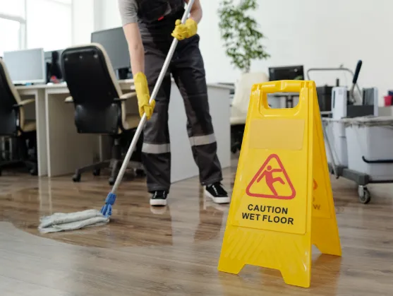 Janitor mopping with a wet floor sign in front of him